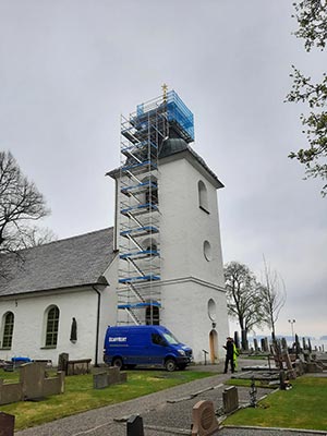 En vit kyrka med byggställning framför tornet